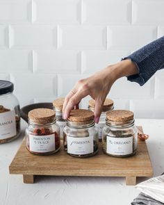 a person reaching for some food in jars on a wooden tray next to other items