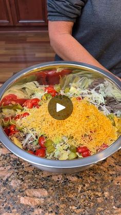 a man standing in front of a metal pan filled with salad and cheese on top of a granite counter