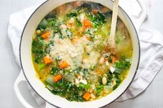 a pot filled with soup and vegetables on top of a white cloth next to a wooden spoon