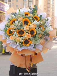 a woman holding a bouquet of sunflowers in her hands on the street with buildings in the background