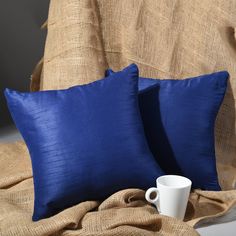 two blue pillows sitting on top of a bed next to a cup and saucer