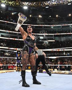 a woman holding up a trophy in the middle of a wrestling ring