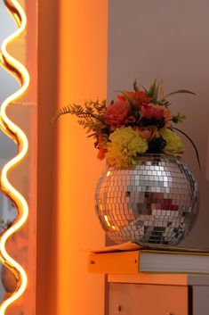 a disco ball with flowers in it sitting on top of a dresser next to a mirror