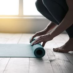 a woman is rolling up a yoga mat on the floor with her hands and feet