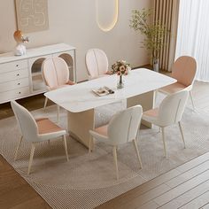 a dining room table with pink chairs and a white rug on the floor in front of it