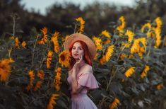 a woman with red hair wearing a straw hat standing in a field of sunflowers