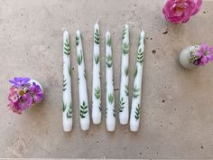 four white candles with green leaves on them next to pink flowers and an easter egg