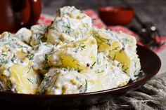 a plate full of potato salad with dill sprigs on top and two cups in the background