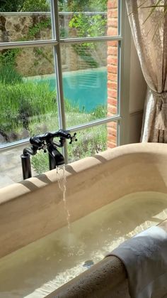 a large bath tub sitting in front of a window next to a lush green field