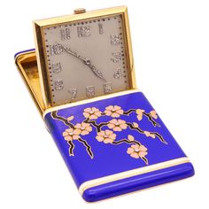 a small blue and gold clock with flowers on it's face in a case