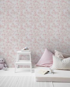 a white bed sitting next to a wall with pink flowers on it and a teddy bear