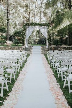 an outdoor wedding ceremony with white chairs and flowers on the aisle, surrounded by greenery