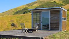 two chairs are sitting on a wooden deck in front of a small cabin with sliding glass doors