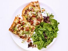 two slices of pizza sitting on top of a white plate next to a green salad