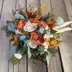 an arrangement of flowers and foliage on a wooden surface