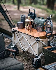 an outdoor table with many items on it in the woods next to a camper