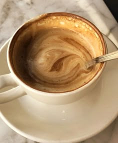 a cup of coffee on a saucer with a spoon in it and marble counter top