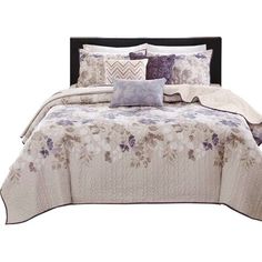 a bed with purple and white flowers on it, along with two throw pillows in the middle