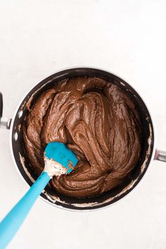 a blue spatula in a pan filled with chocolate frosting on top of a white table