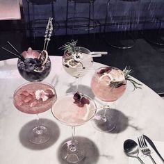 four glasses filled with drinks sitting on top of a table next to utensils