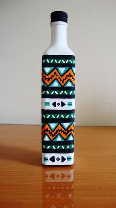 a bottle sitting on top of a wooden table next to a white vase with an orange and blue design