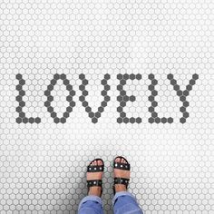 a person standing in front of a tile wall with the word lovely written on it