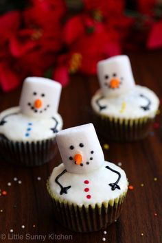 three frosted cupcakes with snowmen on them sitting on a wooden table