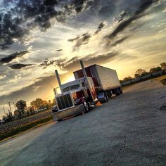 a semi truck is parked on the side of the road in front of a cloudy sky