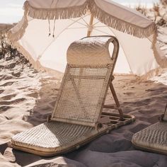 two lawn chairs sitting on top of a sandy beach next to an open white umbrella