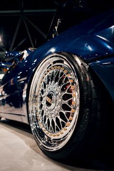 the front wheel of a blue car with chrome rims and spokes on display