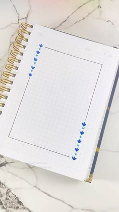 an open notebook with blue hearts on it sitting on a marble surface next to a pen