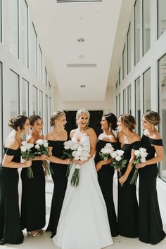 a group of women standing next to each other in front of a window holding bouquets