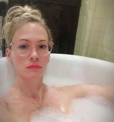 a woman wearing glasses sitting in a bathtub filled with foamy water and bubbles