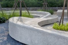 a concrete bench sitting next to a forest filled with lots of green plants and trees