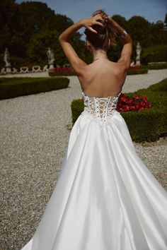 a woman in a white wedding dress is looking back at the camera with her hand on her head