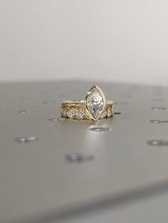 two gold wedding bands with a pear shaped diamond set on top of each other in front of a white background