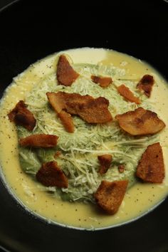 a black bowl filled with soup and croutons on top of a stovetop