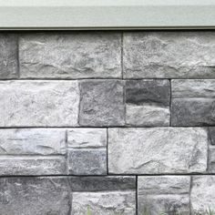 a stone wall with grass growing in the foreground and an open window above it