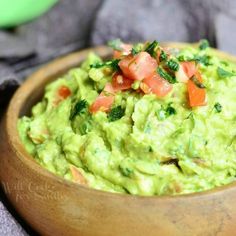 a wooden bowl filled with guacamole and tomatoes