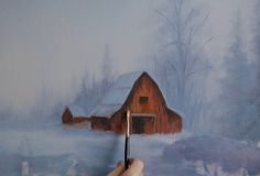 a person is painting a barn in the snow with a pencil and watercolor paints