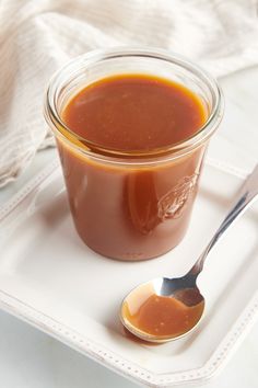 a glass jar filled with sauce on top of a white plate next to a spoon