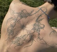 a man with tattoos on his back sitting in the grass