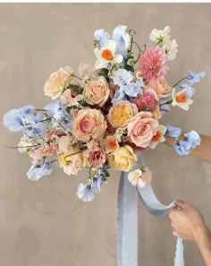 a bouquet of flowers is being held up by someone's hand with a blue ribbon