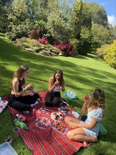 three women sitting on the grass eating and drinking