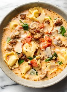 a bowl filled with pasta, meat and vegetables on top of a marble countertop