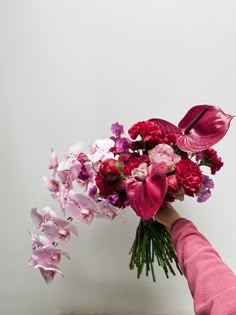 a person holding a bouquet of flowers on top of a wooden table in front of a white wall