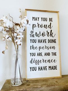 a vase filled with cotton flowers next to a framed sign that says, may you be proud of the work you have done