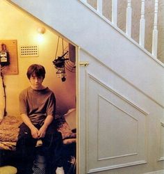 a young man sitting on top of a bed under a stair case