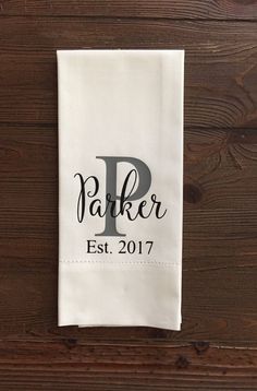 a personalized tea towel hanging on a wooden wall with the word parker est 2017 printed on it