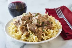 a white plate topped with pasta covered in meat and gravy next to a glass of red wine